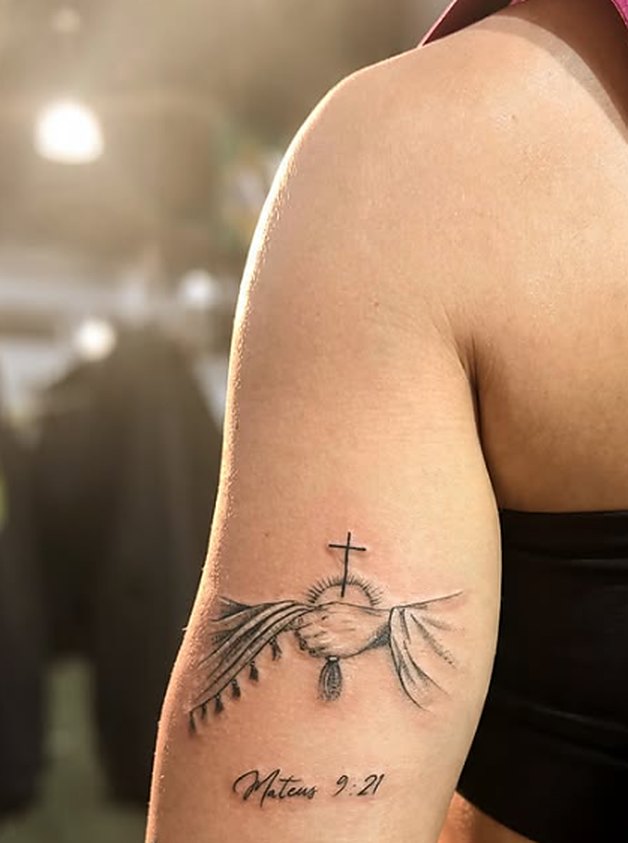 Tatuagem fineline de mãos em oração com cruz e versículo